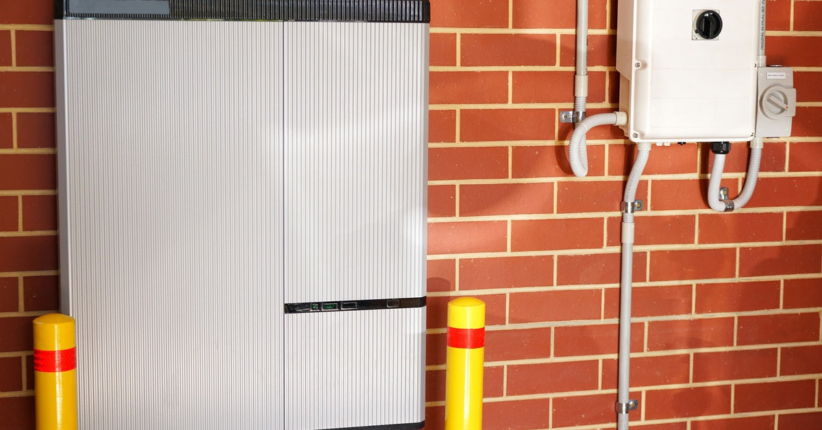 A large lithium-ion solar battery system next to two yellow posts. The system is installed on a brick wall.